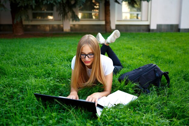 Jeune fille allongée sur l&#39;herbe dans le parc, étudiant avec un ordinateur portable