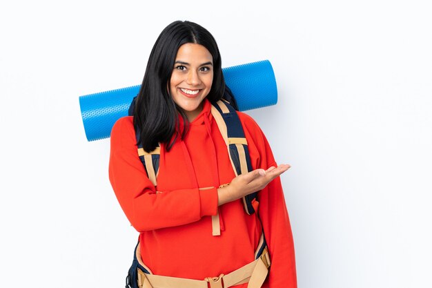 Jeune fille alpiniste avec un grand sac à dos isolé sur blanc, étendant les mains sur le côté pour inviter à venir