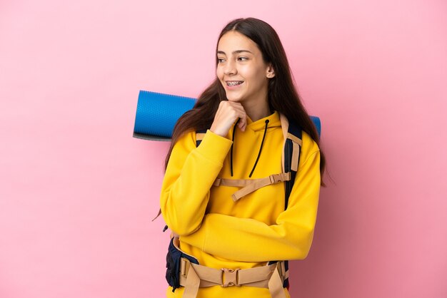 Photo jeune fille d'alpiniste avec un gros sac à dos isolé sur fond rose à la recherche sur le côté et souriant