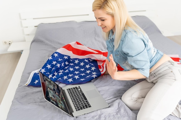 Une jeune fille américaine diffuse en direct avec son ordinateur portable. Drapeau américain en arrière-plan. Concept de vlogger.