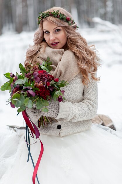 Une jeune fille d'apparence slave avec une couronne de fleurs sauvages. Belle mariée blonde tient un bouquet en fond d'hiver.