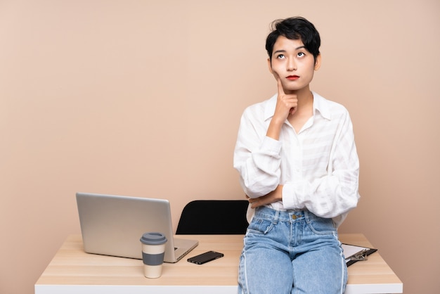 Jeune fille asiatique d'affaires dans son lieu de travail en pensant à une idée