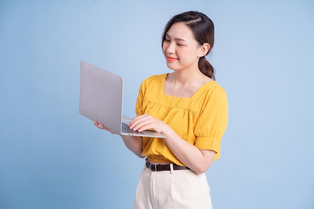 Jeune fille asiatique à l'aide d'un ordinateur portable sur fond bleu