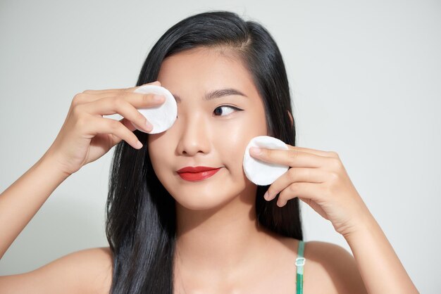 Photo une jeune fille asiatique en bonne santé enlevant le maquillage de son visage avec un tampon de coton souriant