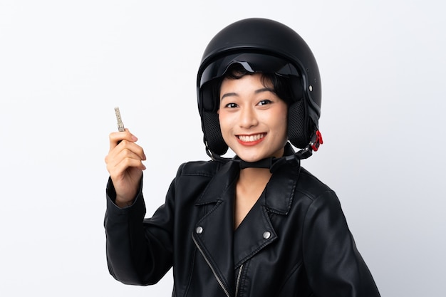 Jeune fille asiatique avec un casque de moto et une clé sur un mur blanc isolé