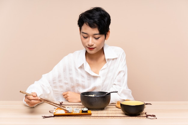 Jeune fille asiatique dans une table avec bol de nouilles et sushi