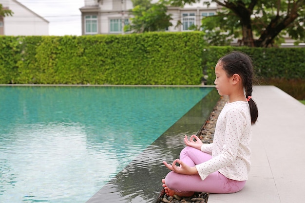 Jeune fille asiatique enfant pratiquant la méditation de pleine conscience assis près de la piscine