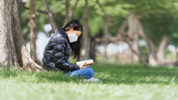 Une jeune fille asiatique a l'intention de lire un livre pour préparer l'examen de test final assis sous les arbres du parc en plein air pendant l'heure d'apprentissage en été. Éducation Apprentissage Étudier le concept.