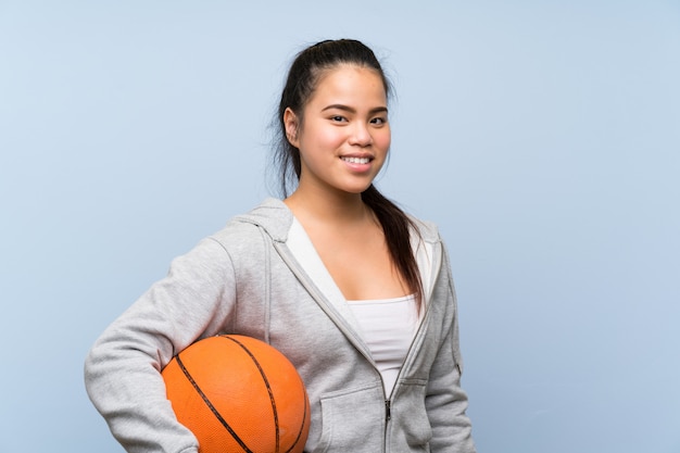 Jeune fille asiatique jouant au basketball sur un mur isolé