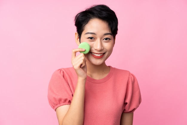 Jeune fille asiatique sur un mur rose isolé tenant des macarons français colorés