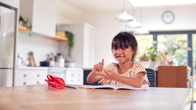 Jeune fille asiatique scolarisation à domicile travaillant à table dans la cuisine en comptant sur les doigts