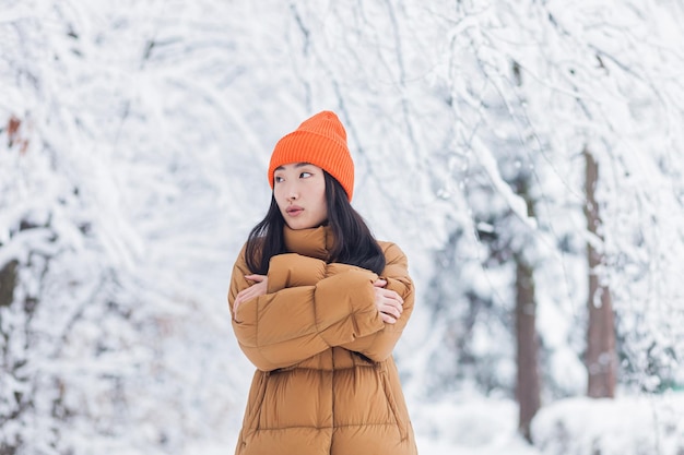 Jeune fille asiatique se fige dans le parc en attendant un rendez-vous un jour de neige d'hiver une femme chaudement vêtue