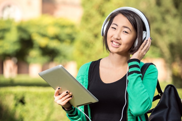 Jeune fille asiatique souriante écoute de la musique avec tablette.