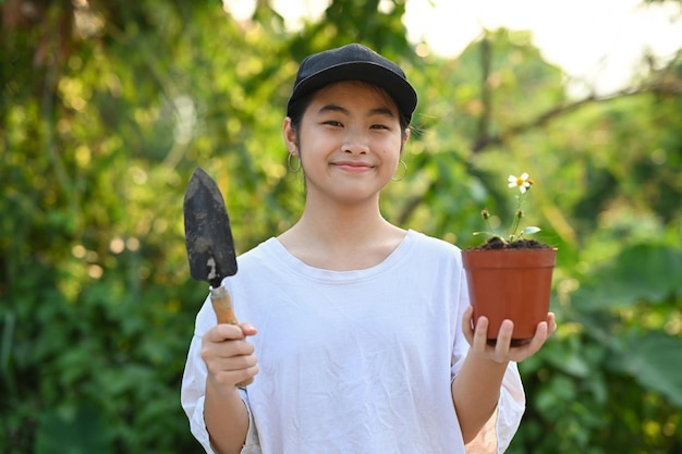 Jeune fille asiatique souriante tenant une pelle de jardin et un pot de fleurs dans les mains Concept de sauver la journée mondiale de la terre