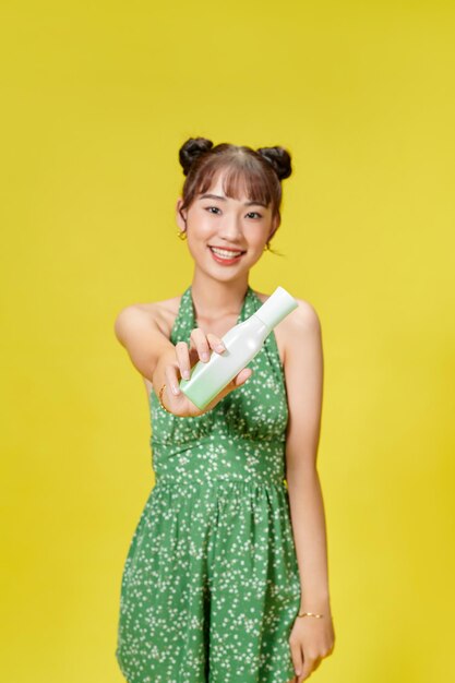 Jeune fille asiatique en studio avec des bouteilles de cosmétiques sur fond jaune