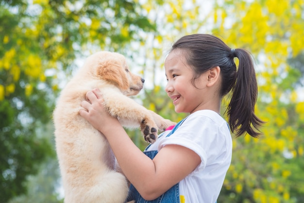 Jeune fille asiatique tenant un petit chien Golden Retriever dans le parc