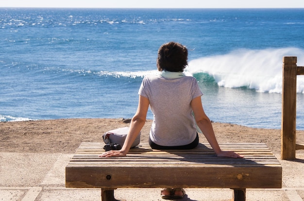 Jeune fille assise sur un banc en bois en contemplant les vagues de la mer au phare de Jandia