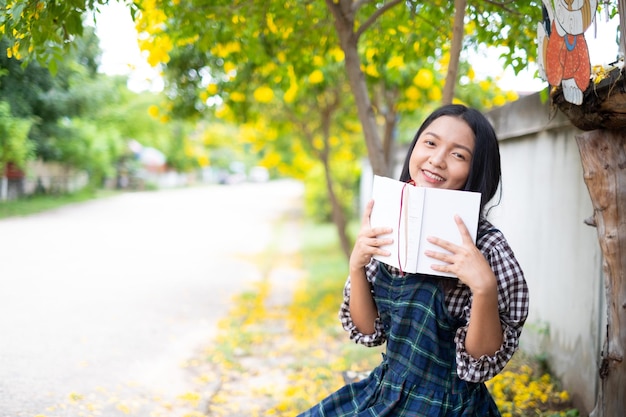 Jeune fille assise sur un banc lisant un livre sous un bel arbre