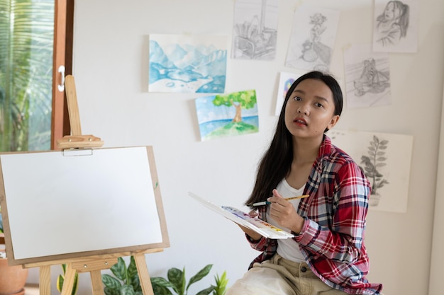 Jeune fille assise sur une chaise avec chevalet pour dessiner la palette de couleurs et le pinceau dans la chambre