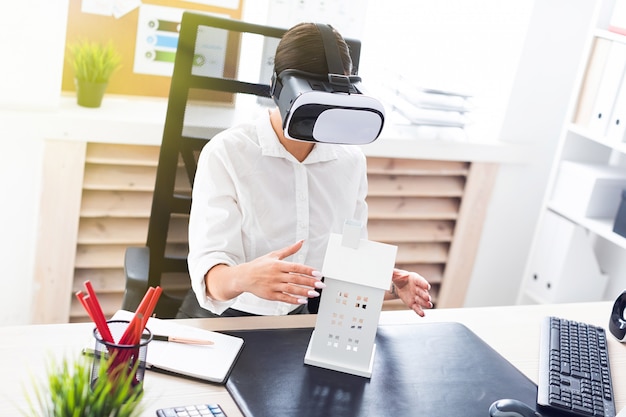 Jeune fille assise dans des lunettes de réalité virtuelle. Devant elle, sur la table, la disposition de la maison.