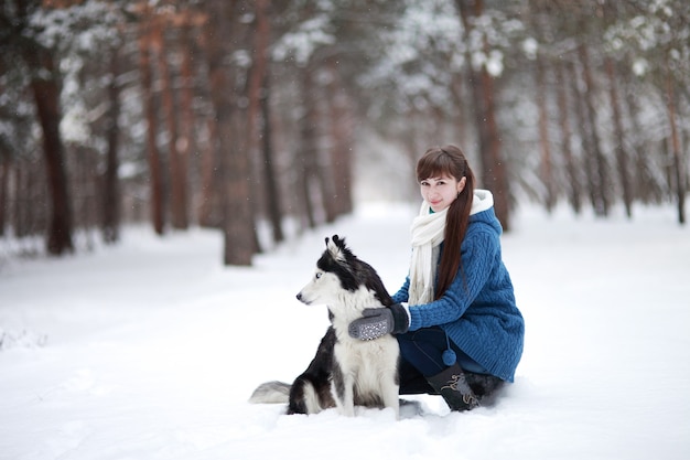 La jeune fille assise dans la neige avec un chien husky sibérien dans la forêt d'hiver