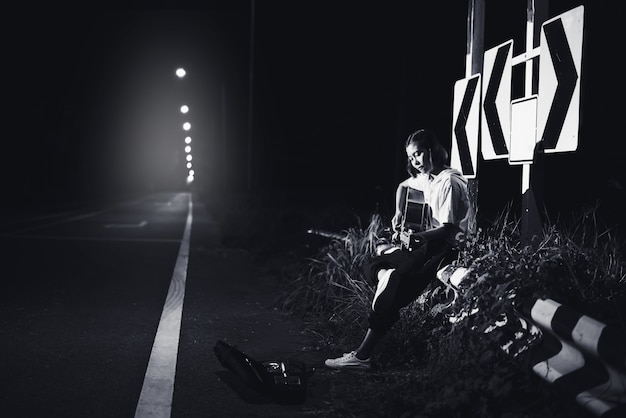 Photo jeune fille assise et jouant de la guitare au bord de la route avec fond de signe de route, voyage du concept de musicien