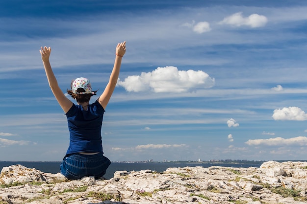 Jeune fille assise sur une pierre avec les mains contre le ciel avec des nuages