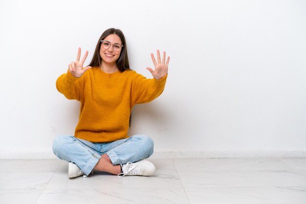 Jeune fille assise sur le sol isolé sur fond blanc comptant huit avec les doigts