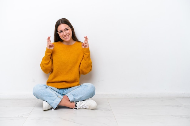 Jeune fille assise sur le sol isolé sur fond blanc avec les doigts croisés