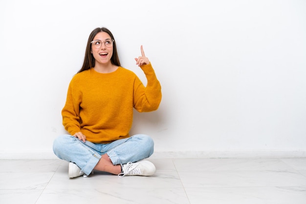 Jeune fille assise sur le sol isolé sur fond blanc pointant vers le haut et surpris