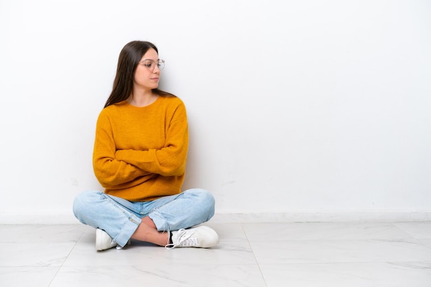 Jeune fille assise sur le sol isolé sur fond blanc en position latérale