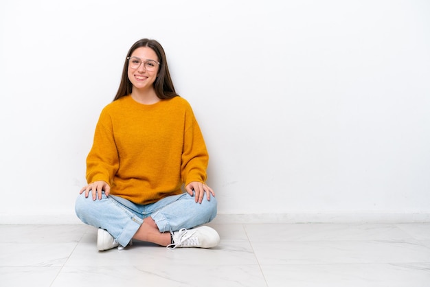 Jeune fille assise sur le sol isolé sur fond blanc en riant