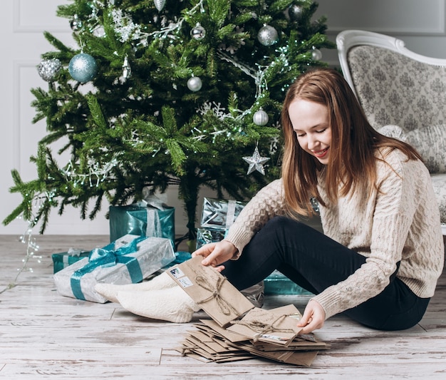 Jeune fille assise sur le sol près de sapin et de lire les lettres de Noël