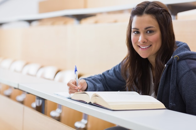 Jeune fille assise en souriant en lisant un livre et en prenant des notes