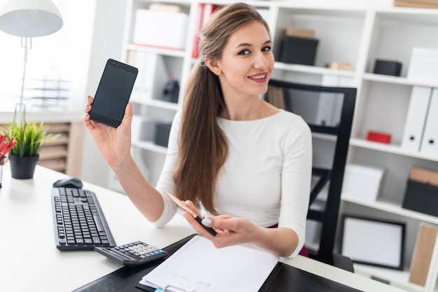 Une jeune fille assise à une table et tenant un téléphone.