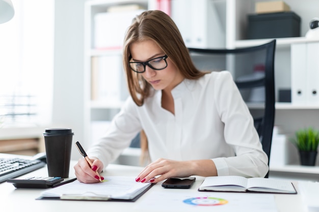 Jeune fille assise à la table et travaillant avec des documents et une calculatrice