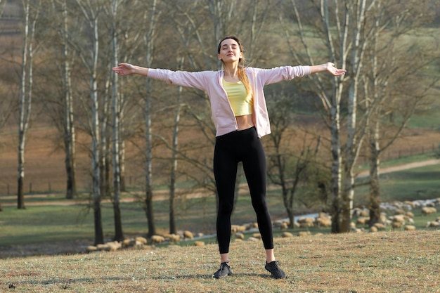 Une jeune fille athlétique mince en tenue de sport effectue une série d'exercices Fitness et mode de vie sain sur fond de collines vertes de pâturages de printemps