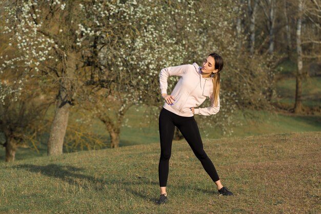 Une jeune fille athlétique mince en tenue de sport effectue une série d'exercices. Remise en forme et mode de vie sain dans le contexte des collines vertes des pâturages de printemps.