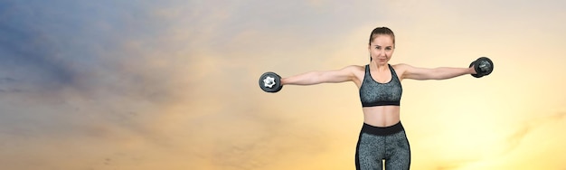 Une jeune fille athlétique mince en vêtements de sport effectue une série d'exercices contre le coucher du soleil au bord de la mer Effectue des exercices avec des haltères Fitness et mode de vie sain