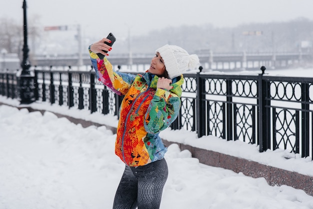 Une jeune fille athlétique prend un selfie un jour glacial et neigeux. Fitness, loisirs.