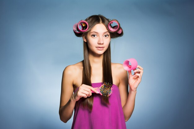 La jeune fille attirante fait une coiffure à la mode avec de grands bigoudis et peignes