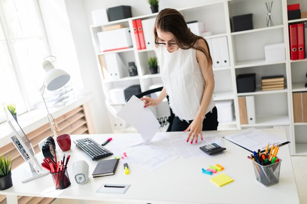 Une jeune fille au bureau se tient près de la table et regarde des documents.