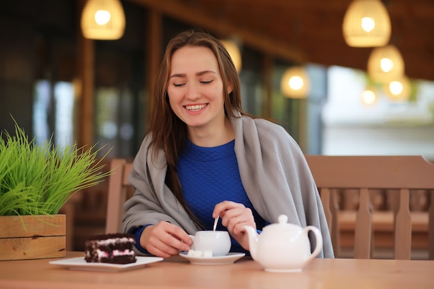 Jeune fille au café s'assoit et boit du thé avec un dessert