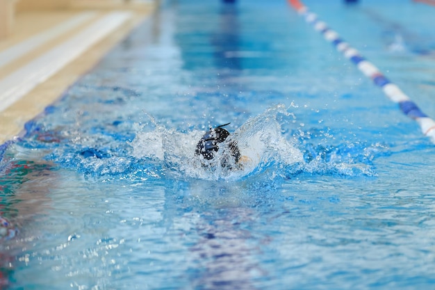 Jeune fille au chapeau nageant dans la piscine d'eau bleue