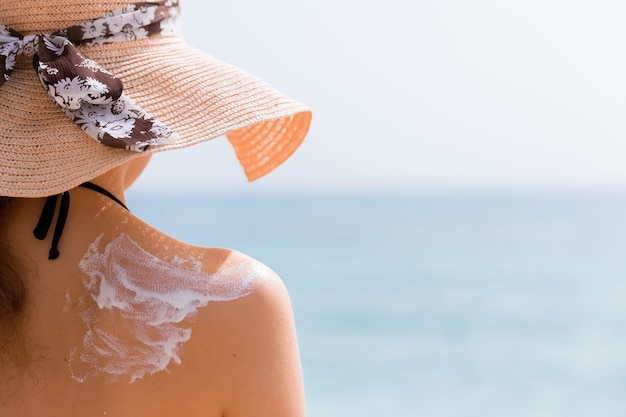 Une jeune fille au chapeau de paille applique un écran solaire sur son dos pour protéger sa peau.