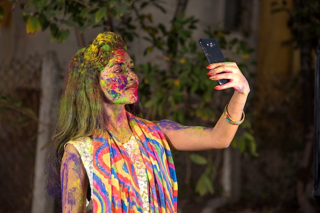 Jeune fille au visage coloré prenant selfie à l'aide de smartphone sur Holi festival. Concept de festival et de technologie