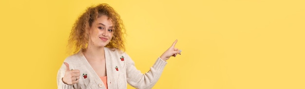 Une jeune fille aux cheveux bouclés pointe d'un geste sur un fond de studio