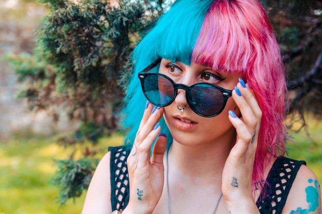 Jeune fille aux cheveux colorés en bleu et rose tenant une paire de lunettes de soleil