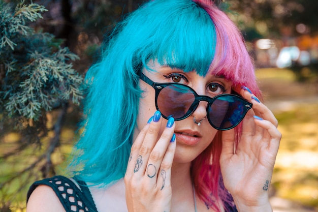 Jeune fille aux cheveux colorés en bleu et rose tenant une paire de lunettes de soleil