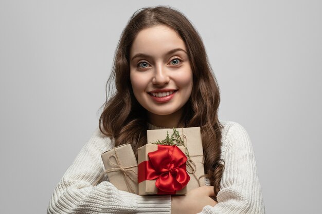 Une jeune fille aux cheveux longs et un cadeau dans ses mains, souriante et regardant directement la caméra